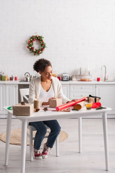 Smiling african american woman looking at gift box and christmas decor at home — Stock Photo