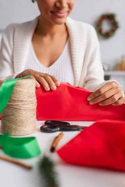 Cropped view of blurred african american woman wrapping gift near twine and cinnamon sticks — Stock Photo