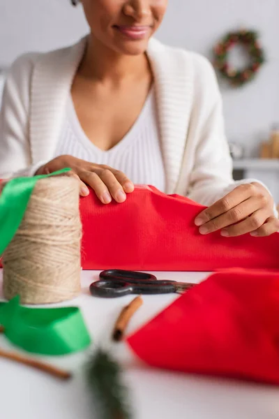 Ausgeschnittene Ansicht einer verschwommenen afrikanisch-amerikanischen Frau, die Geschenk in der Nähe von Bindfäden und Zimtstangen einwickelt — Stockfoto