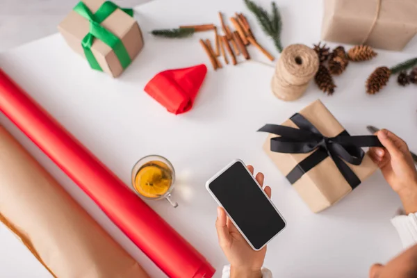 Top view of african american woman holding smartphone while decorating christmas gift at home — Stock Photo
