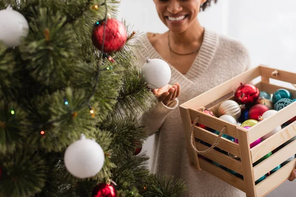 Vista recortada del árbol de navidad cerca de la borrosa mujer afroamericana con adornos en casa - foto de stock