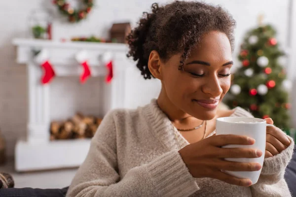 Smiling african american woman holding cup during christmas at home — Stock Photo