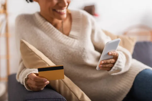 Vista cortada da mulher americana africana sorrindo usando celular e cartão de crédito em casa — Fotografia de Stock