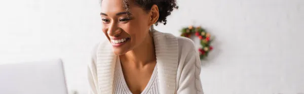 Mujer afroamericana positiva usando el ordenador portátil durante la Navidad en casa, bandera - foto de stock