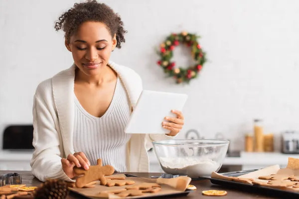 Afroamerikanerin hält digitales Tablet in der Nähe von Lebkuchen und Mehl in der Küche — Stockfoto