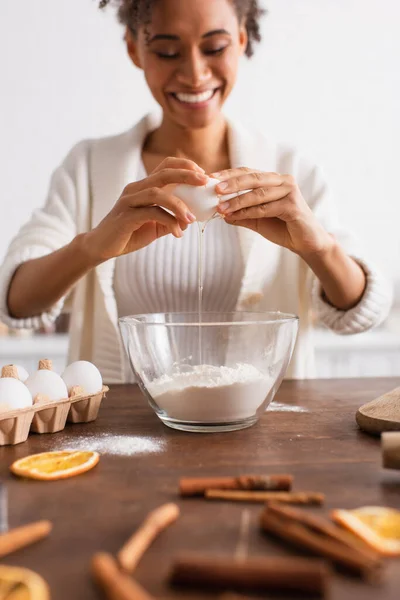 Blurred african american woman pouring egg in flour near cinnamon sticks in kitchen — Stock Photo