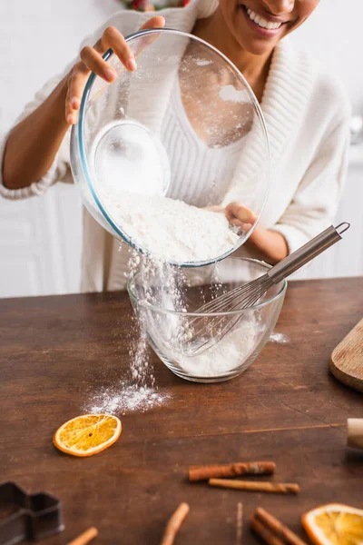 Vista cortada da mulher americana africana derramando farinha perto de laranja seca e paus de canela desfocados — Fotografia de Stock