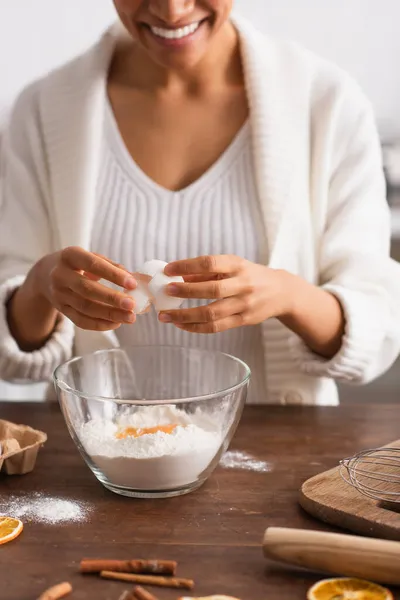 Cropped view of blurred african american woman pouring egg in flour near cinnamon sticks in kitchen — Stock Photo