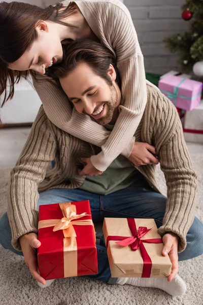 Усміхнена жінка обіймає щасливого чоловіка, сидячи на підлозі з різдвяними подарунками — стокове фото