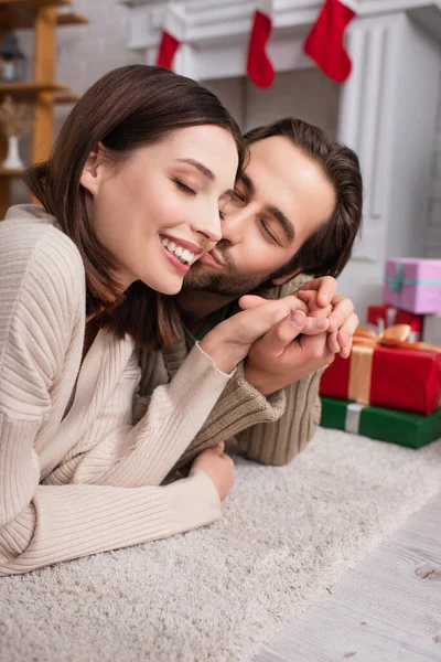 Homme heureux avec les yeux fermés embrasser femme sur le sol près des boîtes-cadeaux floues — Photo de stock