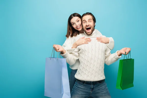 Mulher feliz abraçando homem emocionado segurando compras em azul — Fotografia de Stock
