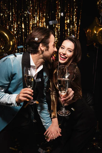 Man sticking out tongue near cheerful woman during christmas party on black — Stock Photo