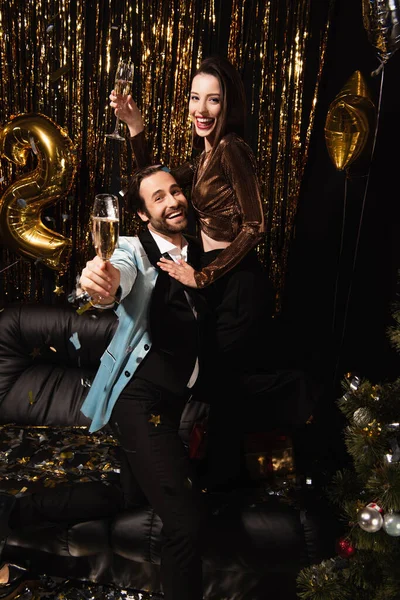 Happy couple holding champagne glasses during christmas party on black — Stock Photo