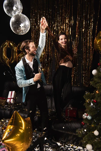 Excited couple with champagne glasses holding hands while celebrating christmas on black — Stock Photo