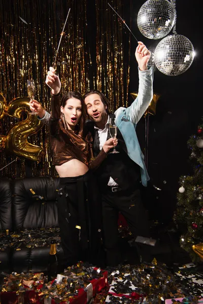 Thrilled couple with sparklers and champagne glasses celebrating christmas on black — Stock Photo