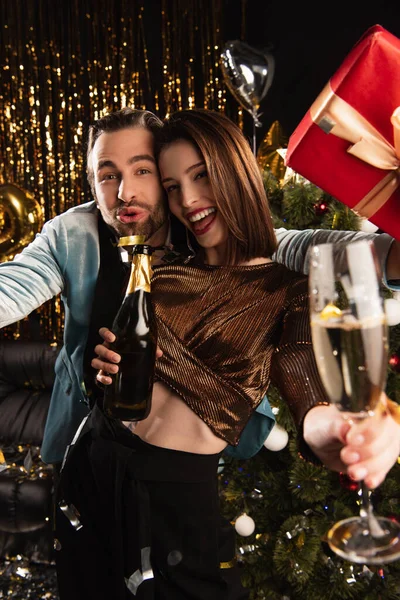 Donna felice in possesso di vetro e bottiglia di champagne vicino uomo entusiasta con Natale presente sul nero — Foto stock