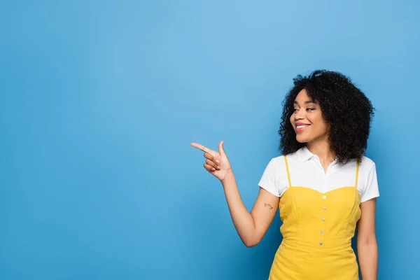 Freudige afrikanisch-amerikanische Frau schaut weg und zeigt mit dem Finger auf blau — Stockfoto