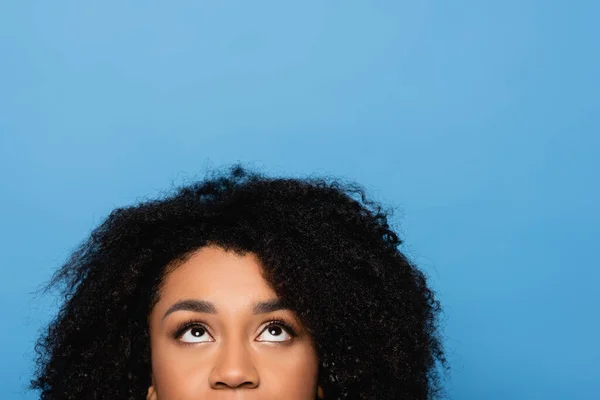 Обрізаний вид на кучеряву афроамериканську жінку, яка дивиться вгору ізольовано на синьому — стокове фото
