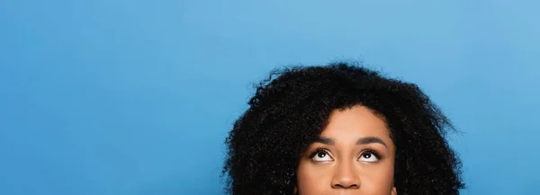 Частковий вид на молоду афроамериканку, яка дивиться вгору ізольовано на синьому, банер — стокове фото