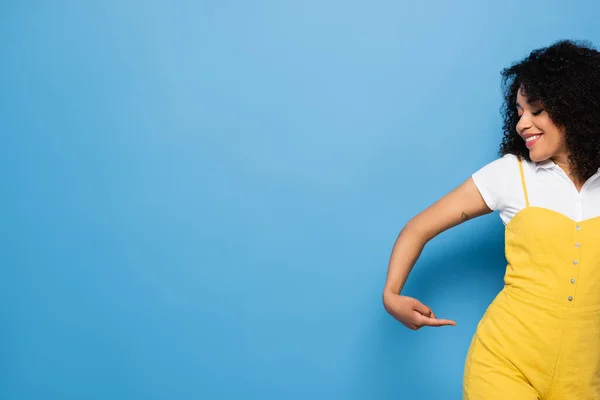 Feliz mulher afro-americana apontando com o dedo para o quadril em azul — Fotografia de Stock