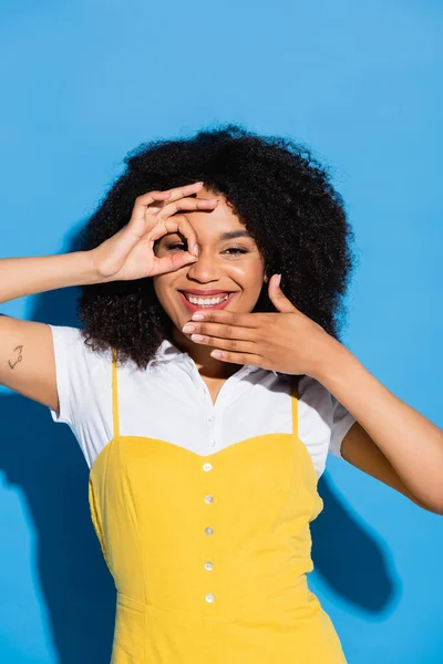 Joyeuse femme afro-américaine montrant un geste correct près du visage sur le bleu — Photo de stock