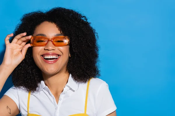 Pleased african american woman in stylish eyeglasses smiling at camera on blue — Stock Photo