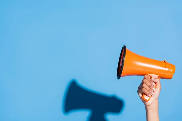 Cropped view of african american woman holding orange megaphone on blue — Stock Photo