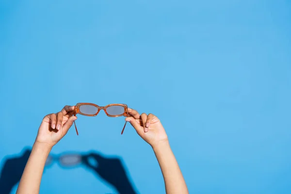 Vue recadrée de femme afro-américaine tenant des lunettes de vue à la mode sur bleu — Photo de stock