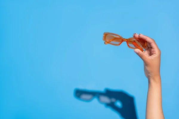 Cropped view of african american woman holding stylish eyeglasses on blue — Stock Photo