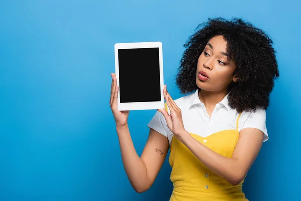 Erstaunt afrikanisch-amerikanische Frau hält digitales Tablet mit leerem Bildschirm auf blau — Stockfoto