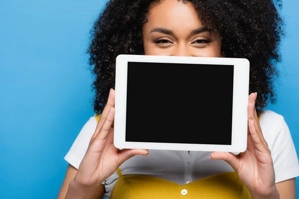 Mujer afroamericana positiva que oscurece la cara con la tableta digital aislada en azul - foto de stock
