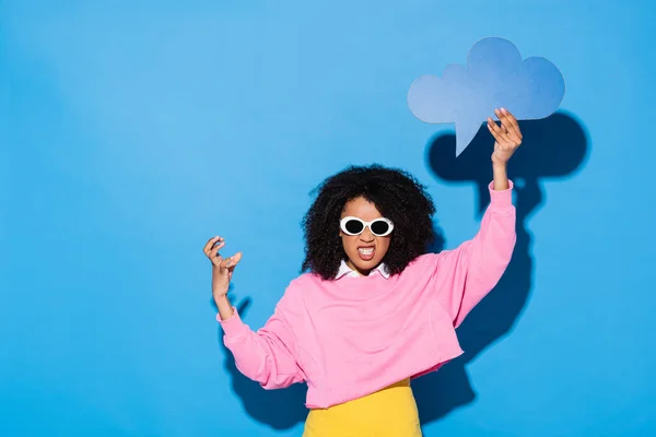 Enojado africano americano mujer con vacío pensamiento burbuja mostrando miedo gesto en azul - foto de stock