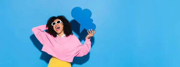 Mujer afroamericana emocionada en ropa de moda sosteniendo la burbuja de pensamiento en azul, bandera - foto de stock