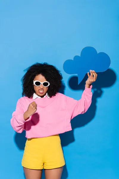 Femme afro-américaine irritée avec bulle de pensée vierge montrant poing sur bleu — Photo de stock