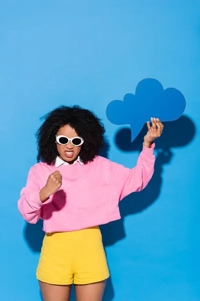 Irritated african american woman with blank thought bubble showing fist on blue — Stock Photo