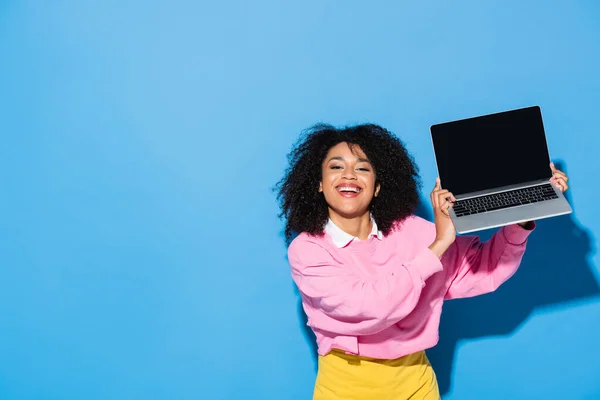 Весела афроамериканка тримає ноутбук з порожнім екраном на синьому — стокове фото