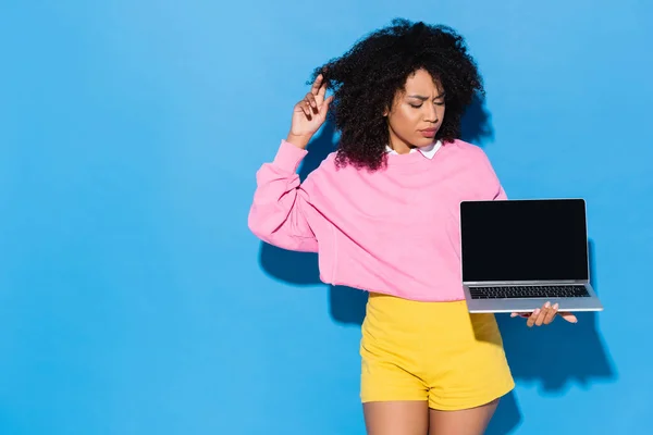 Thoughtful african american woman looking at laptop with blank screen on blue — Stock Photo