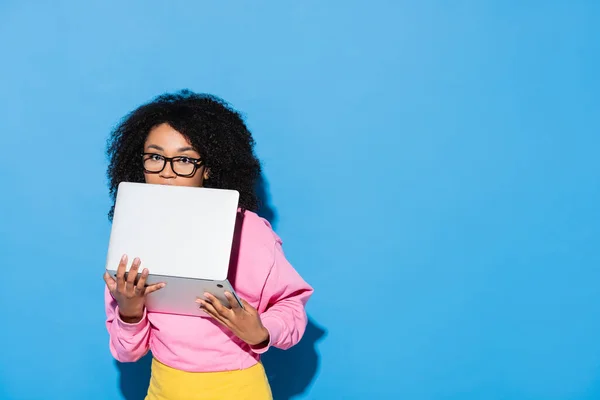 Afroamerikanerin mit Brille verdeckt Gesicht mit Laptop auf blauem Grund — Stockfoto