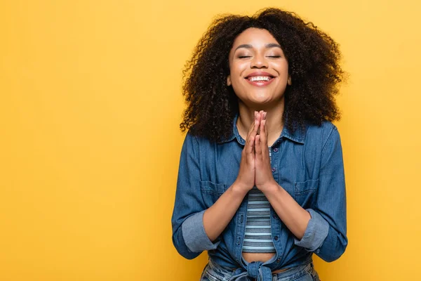 Positivo afroamericano donna con gli occhi chiusi mostrando si prega di gesto isolato su giallo — Foto stock