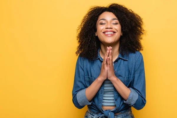 Positive femme afro-américaine avec les yeux fermés montrant s'il vous plaît geste isolé sur jaune — Photo de stock