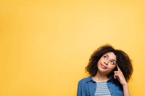 Donna afro-americana pensosa che tocca la testa mentre alza lo sguardo isolato sul giallo — Foto stock