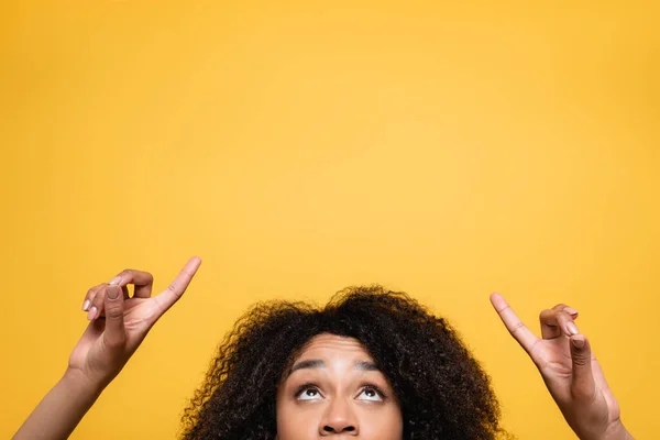 Vista cortada da mulher americana africana olhando para cima e apontando com os dedos isolados no amarelo — Fotografia de Stock