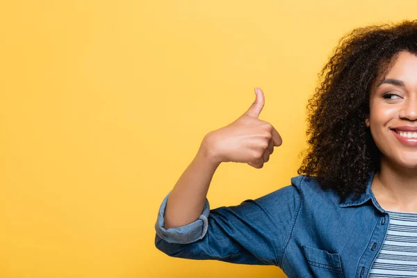 Обрізаний вид веселої афроамериканської жінки, що показує великий палець вгору ізольовано на жовтому — стокове фото