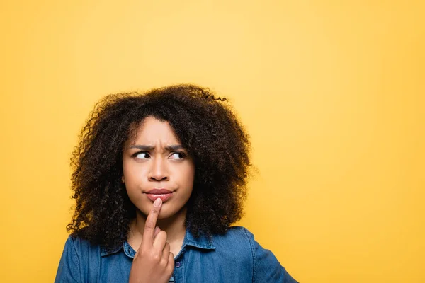 Donna afroamericana premurosa che tocca le labbra e distoglie lo sguardo isolato sul giallo — Foto stock