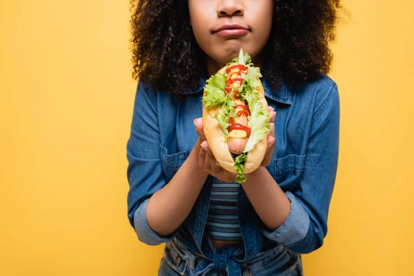 Обрізаний вид афроамериканської жінки, що тримає смачну хот-дог ізольовано на жовтому — стокове фото
