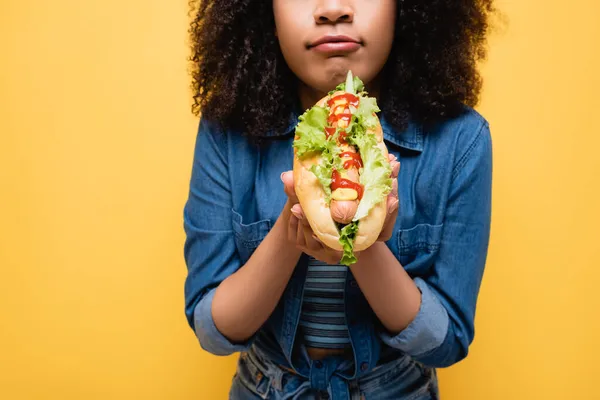 Vista recortada de mujer afroamericana sosteniendo sabroso perrito caliente aislado en amarillo - foto de stock