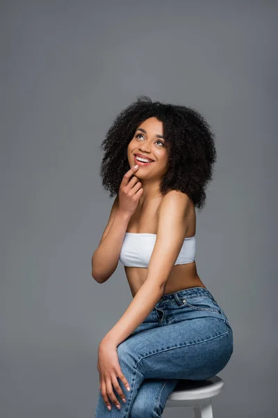 Donna afro-americana sognante con pelle perfetta sorridente mentre alza lo sguardo isolato sul grigio — Foto stock