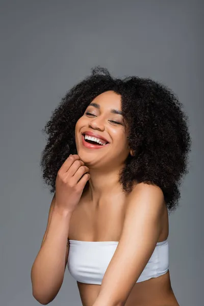 Excited african american woman in white top laughing with closed eyes isolated on grey — Stock Photo