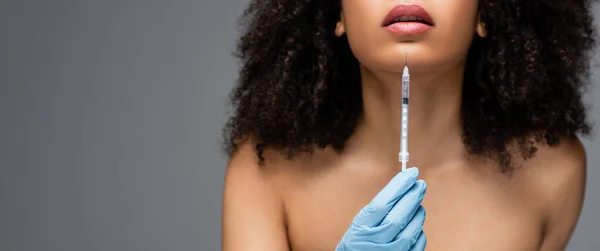 Vue recadrée de la femme afro-américaine en gant de latex tenant la seringue avec injection de beauté isolé sur gris, bannière — Photo de stock