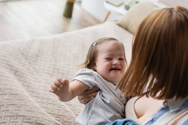 High angle view of woman holding cheerful toddler daughter with down syndrome on bed — Stock Photo